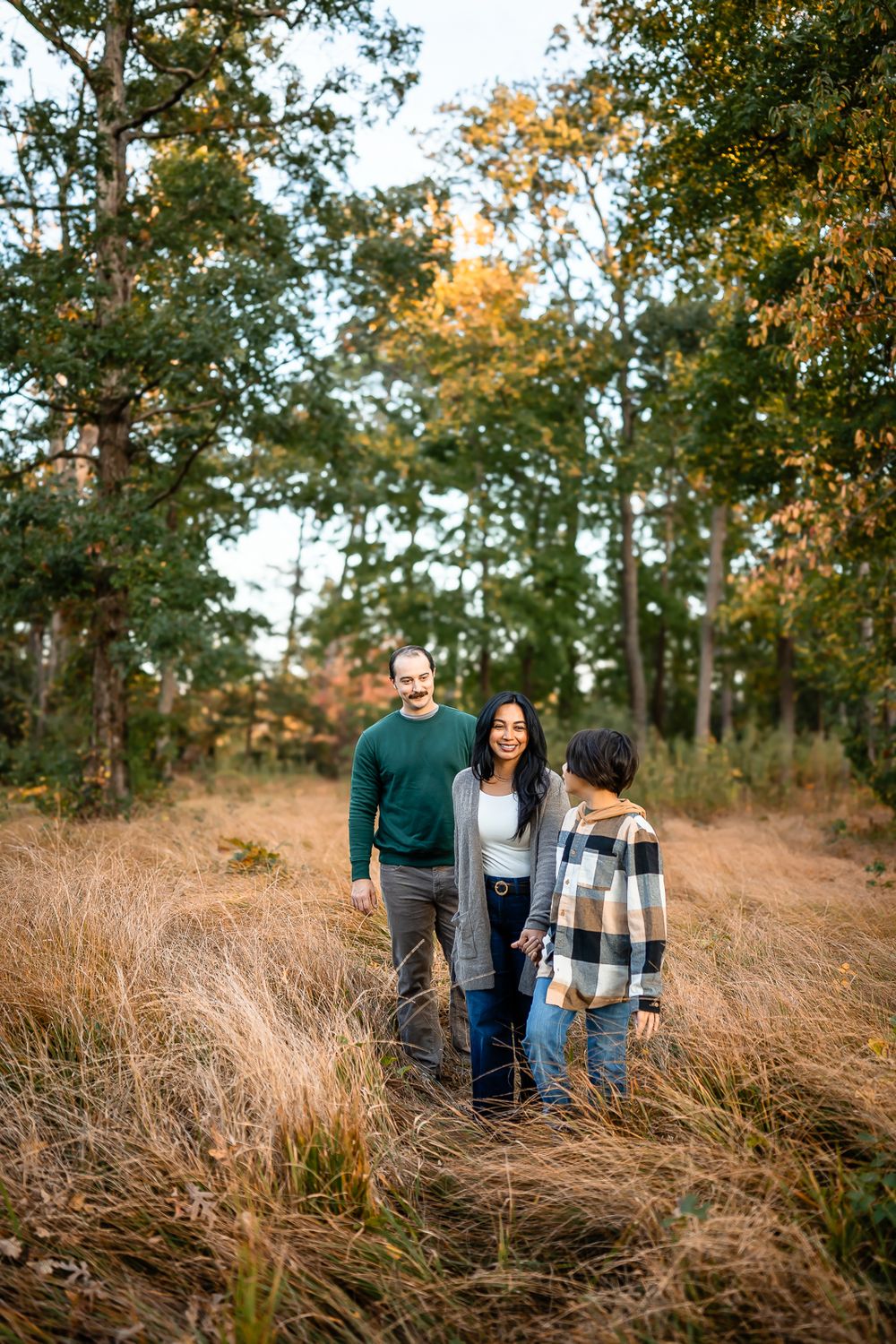 Family standing together in tall grass during golden hour in wooded area.