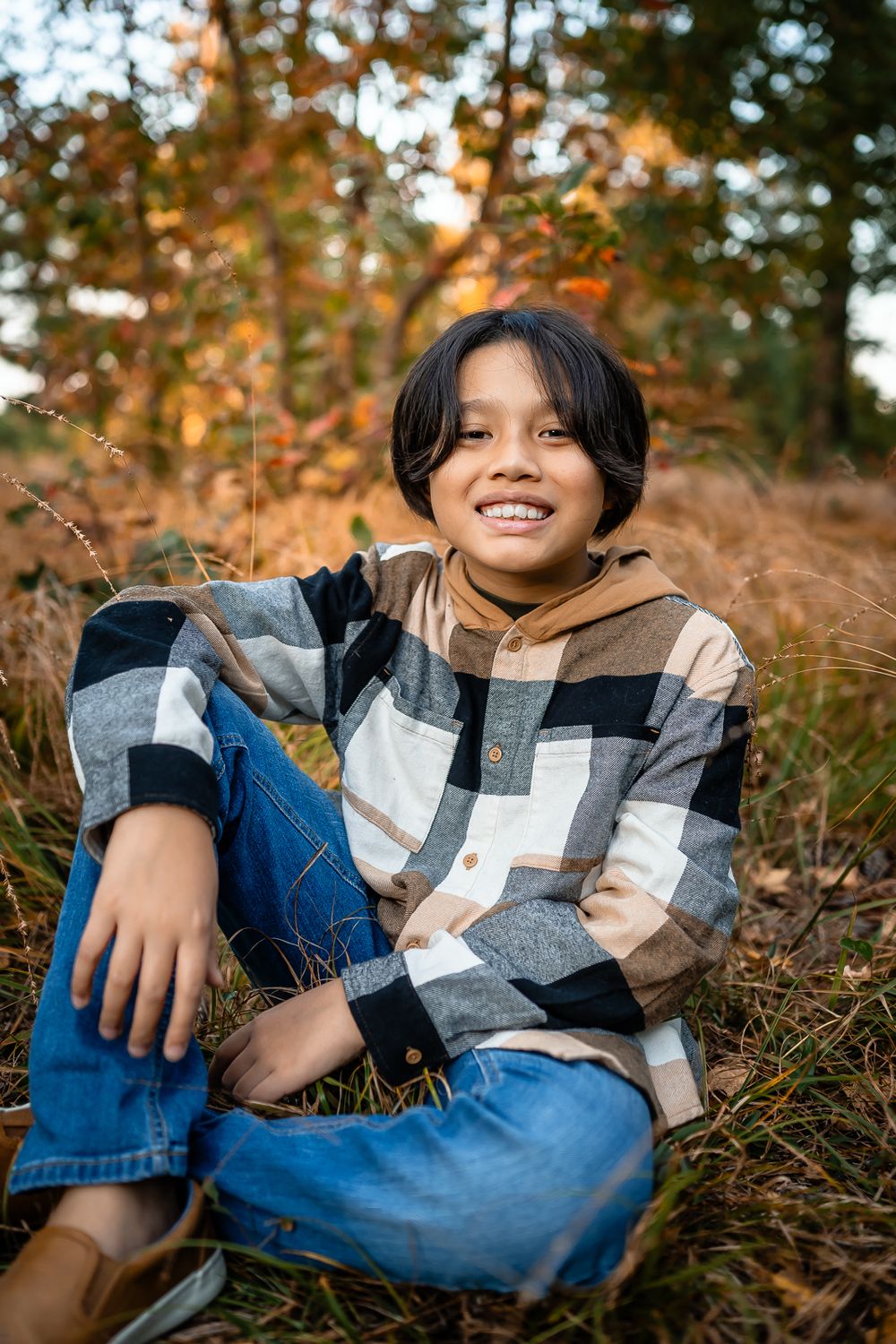 Casual outdoor portrait of young person in plaid jacket sitting in autumn leaves.