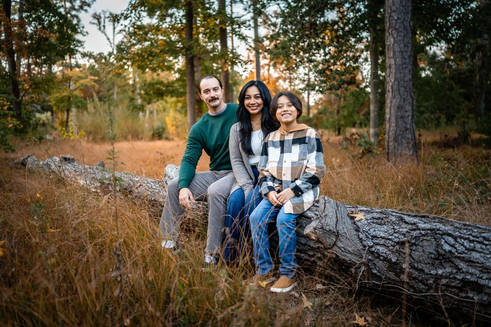 A family sits together on a fallen log surrounded by autumn trees and golden grass.