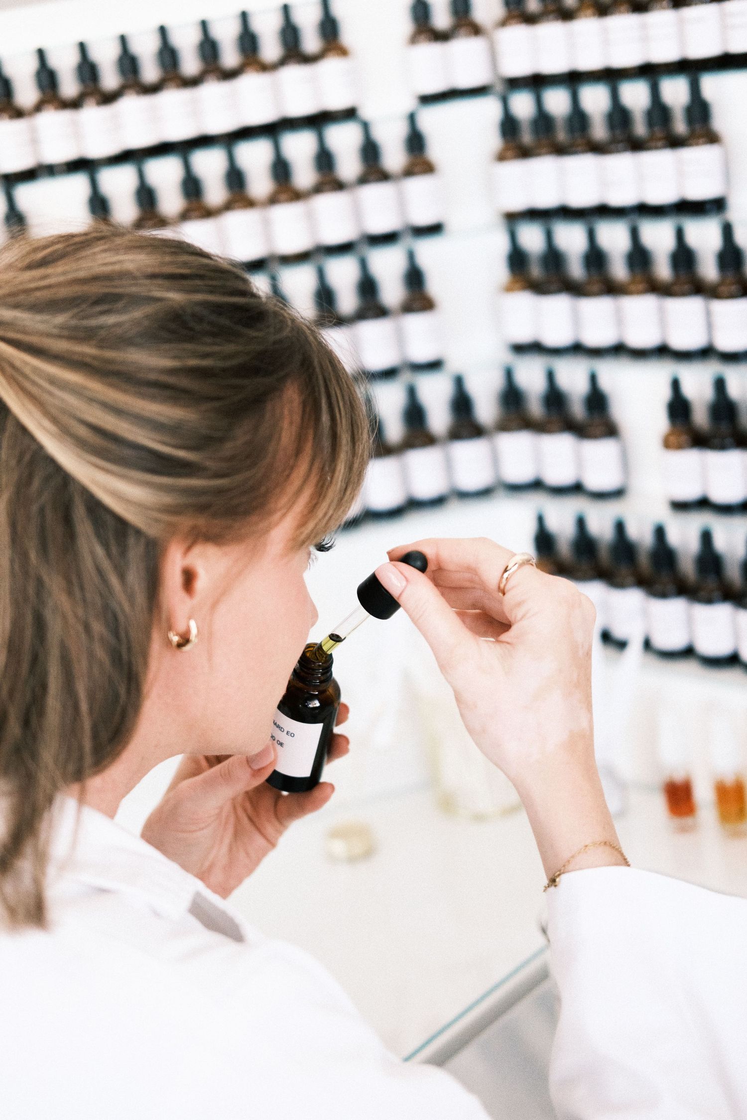 woman in a lab coat smelling essential oil from a small glass bottle