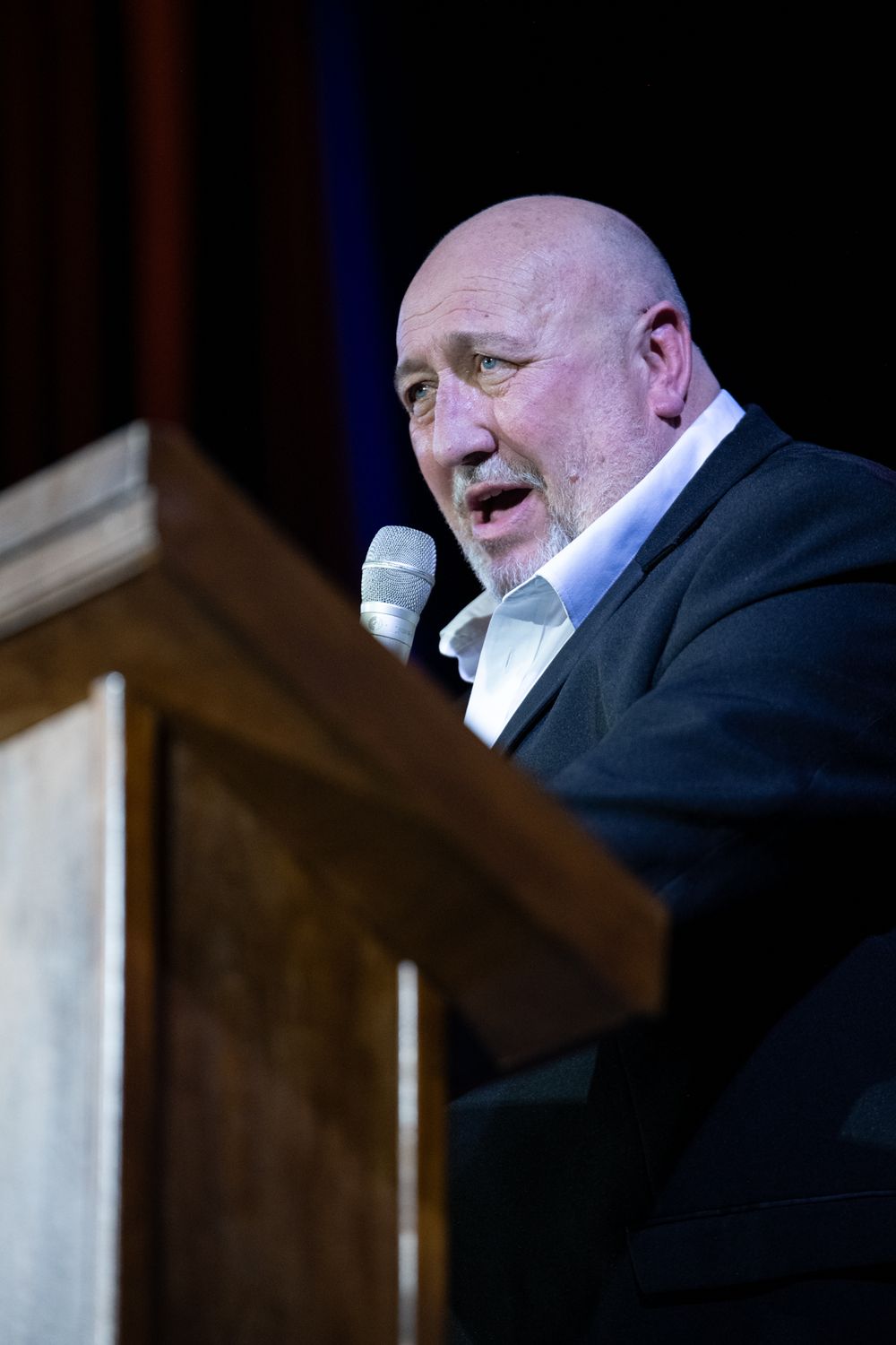 Man in a suit stood on a stage talking to an audience with a mic. Event photography shot in Blackwood, South Wales by K Lewis Photography