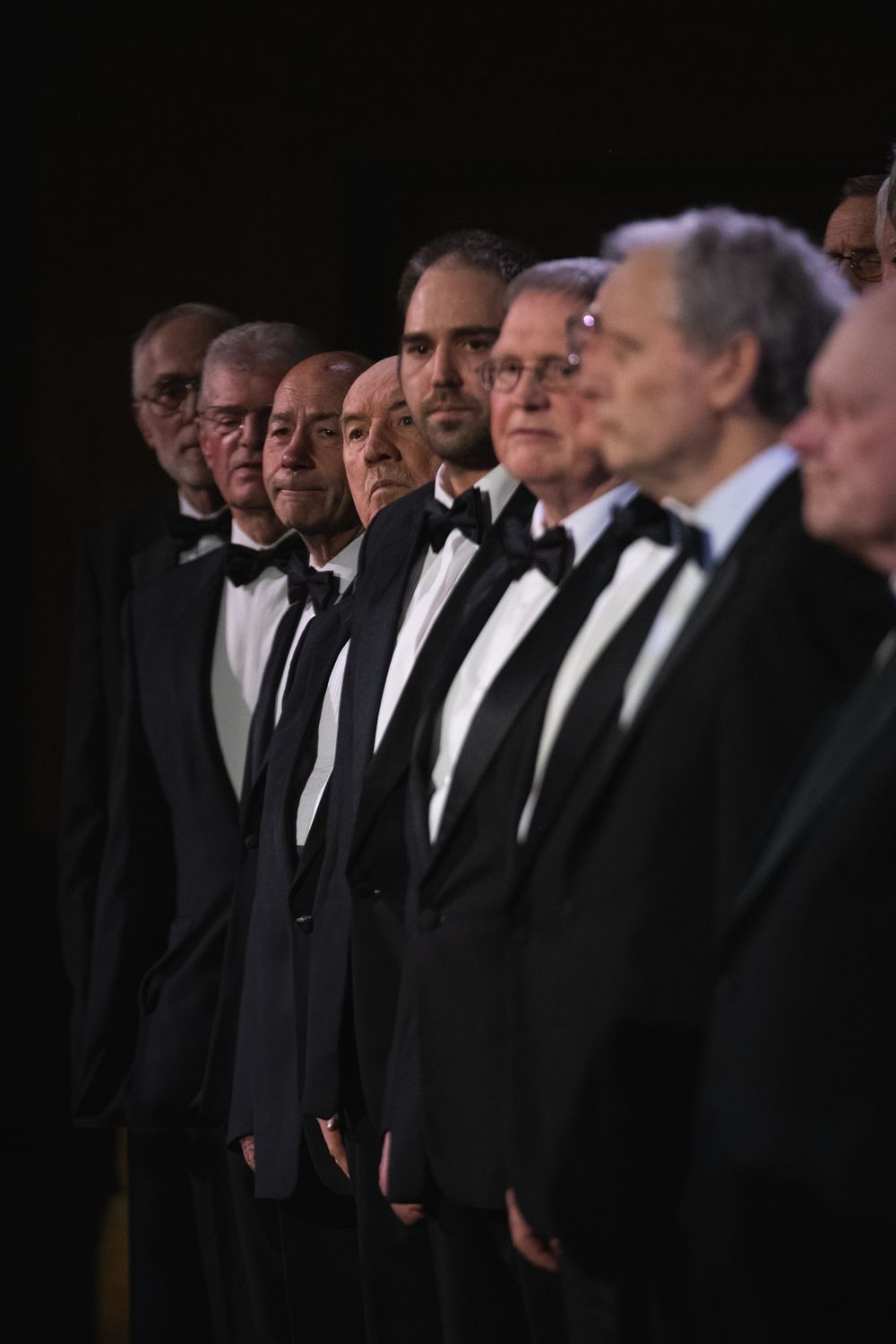 Several members of a male voice choir dressed in black tuxedos taken from a side angle. Shot in Blackwood, South Wales