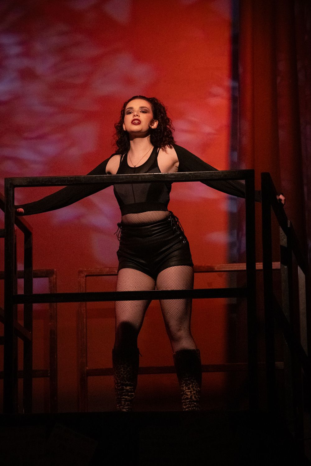 Female performer on stage in black outfit under dramatic red lighting.