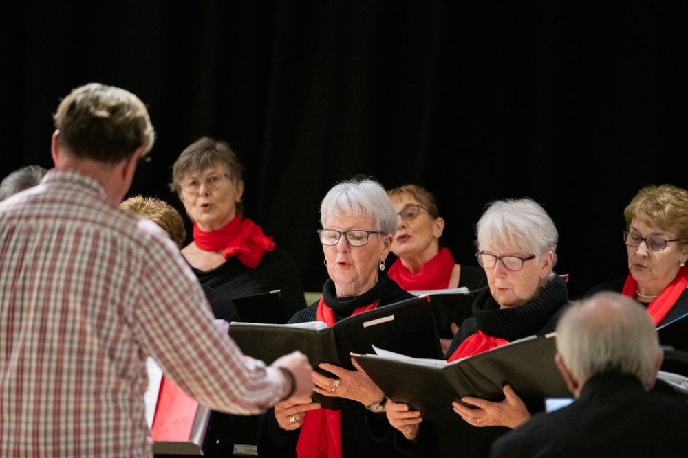 several members of a lady's choir dressed in black with red neck scarfs singing while holding song books. Captured in Newbridge, South Wales