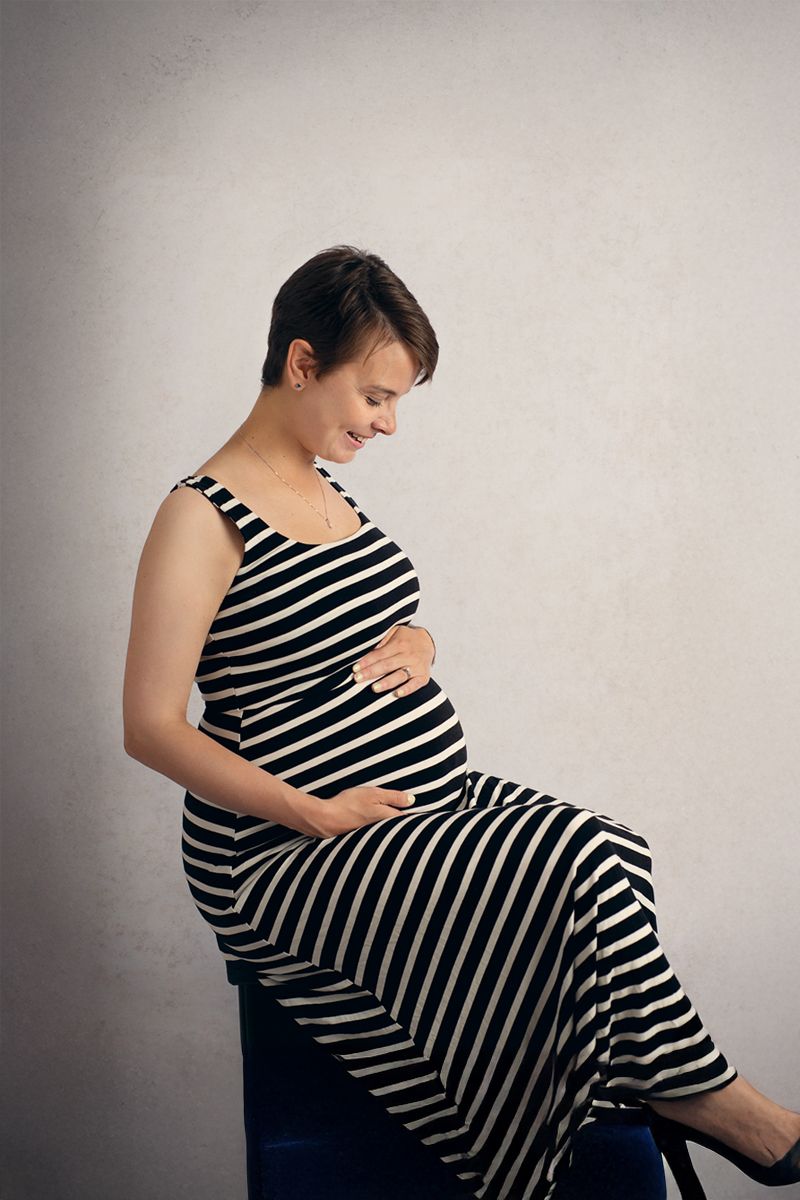 Expecting mother to be sits on a stool holding her belly smiling at her growing belly.