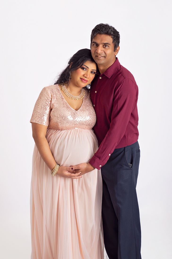 in studio portrait of loving husband and wife hug and lean into each other cradling wife's pregnant belly. Cobourg Ontario*