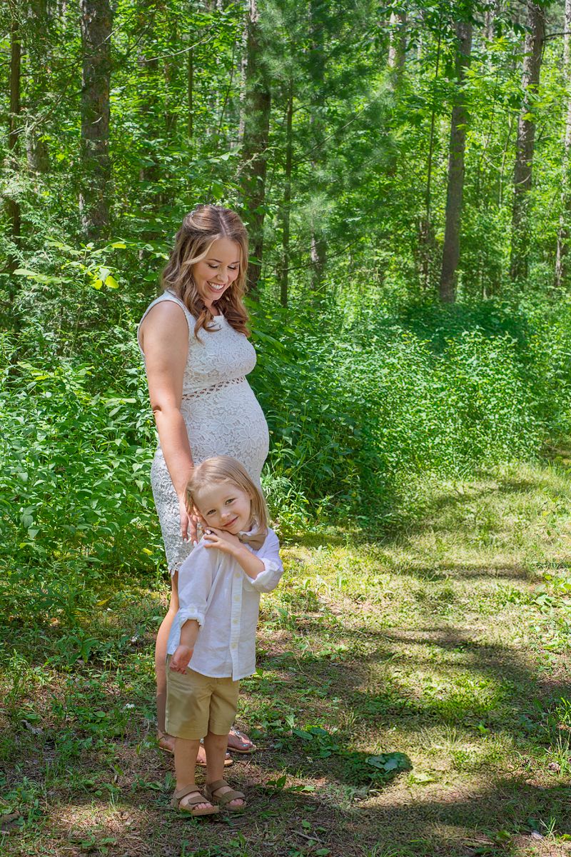 pregnant mother and son stand together naturally posing in Northumberland forest in summer for outdoor maternity session.*