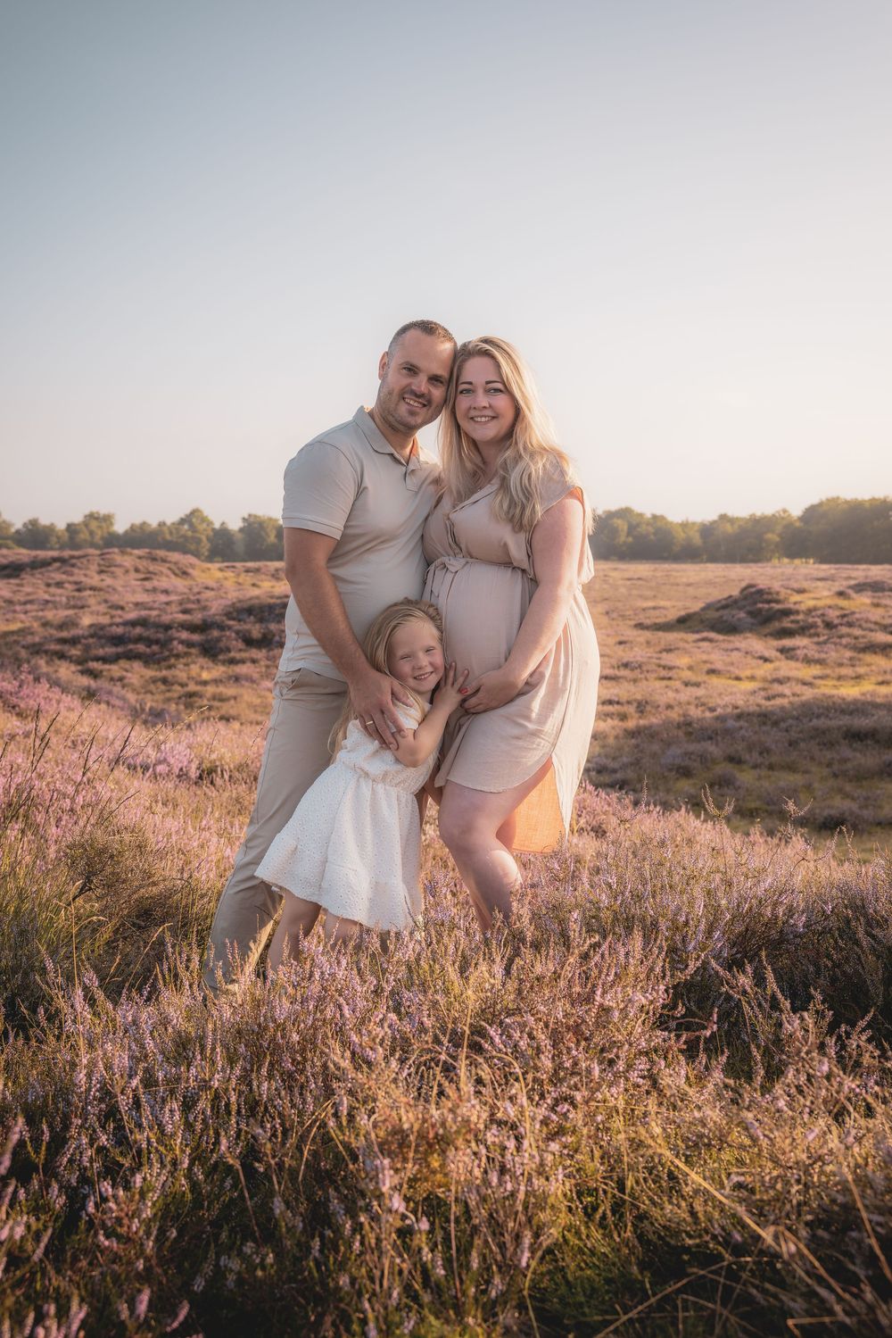 A family poses together in a field of purple heather during golden hour sunset.
