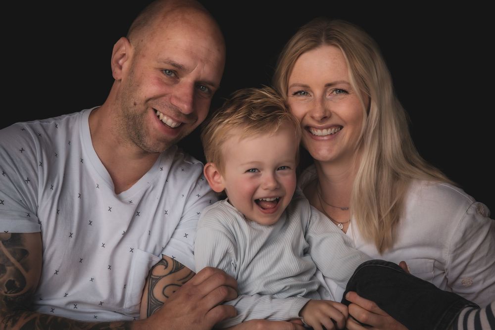 A joyful family wearing white shirts shares loving moments together in a black and white photo series.
