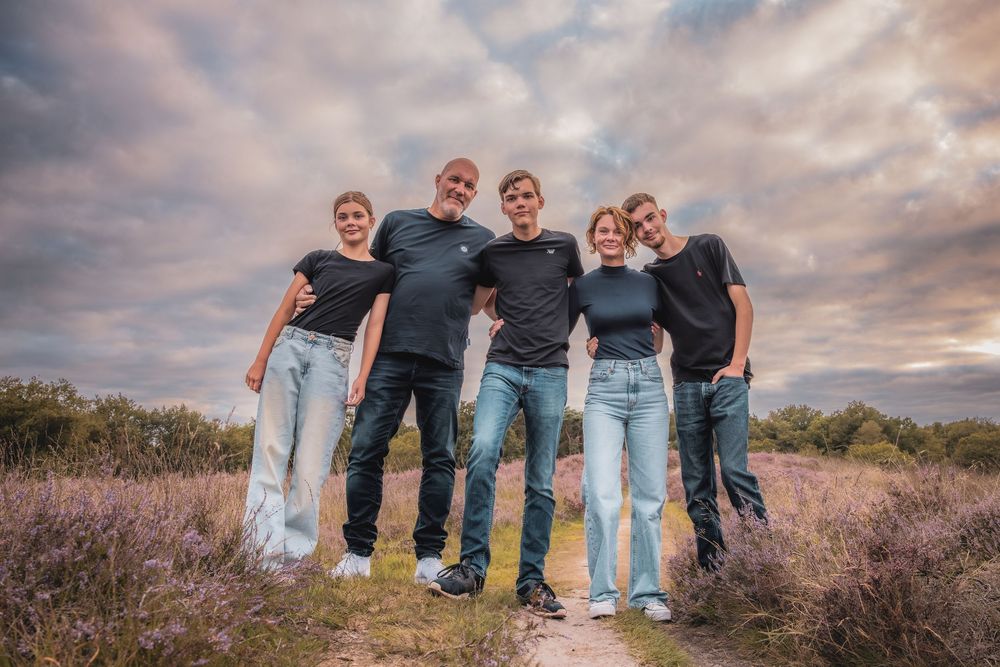 A group stands together on a hilltop path at sunset with dramatic clouds and purple wildflowers in the background.