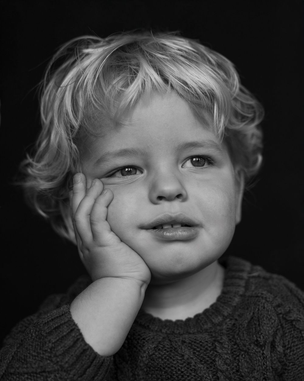 A series of black and white portraits showing a child's playful expressions while resting their face on their hands.