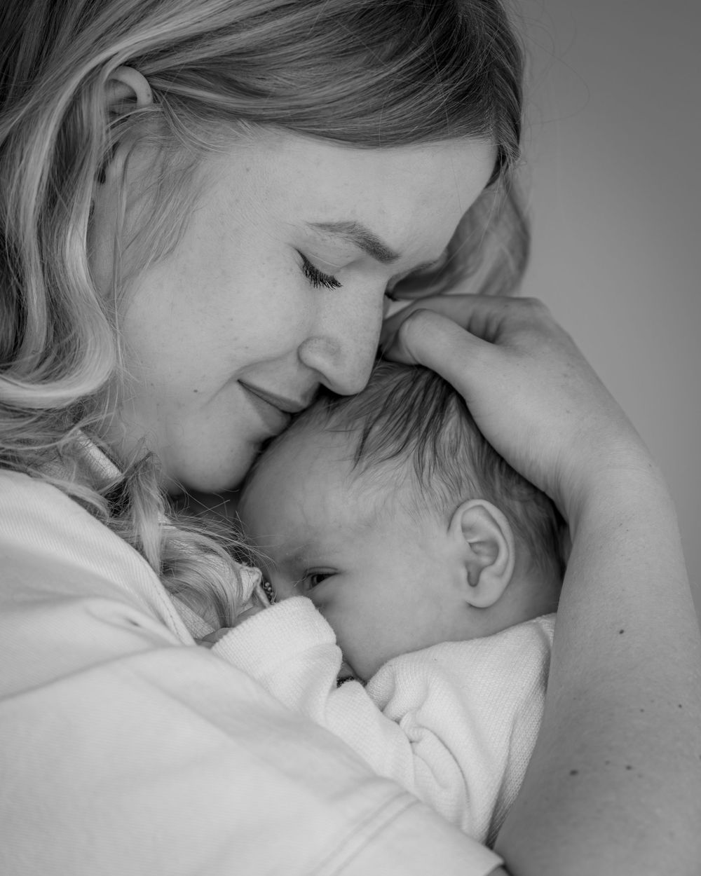 Black and white photo of a smiling mother tenderly cradling her newborn baby close to her face.