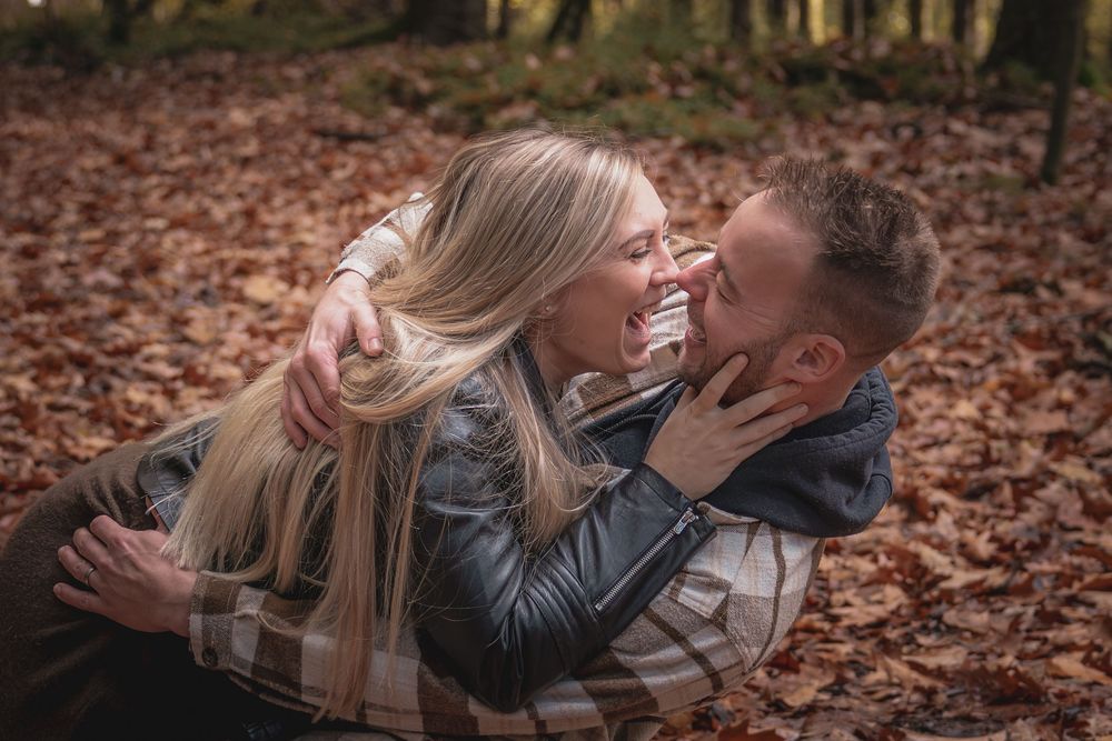A couple shares romantic moments while lying in autumn leaves during a fall photo session.