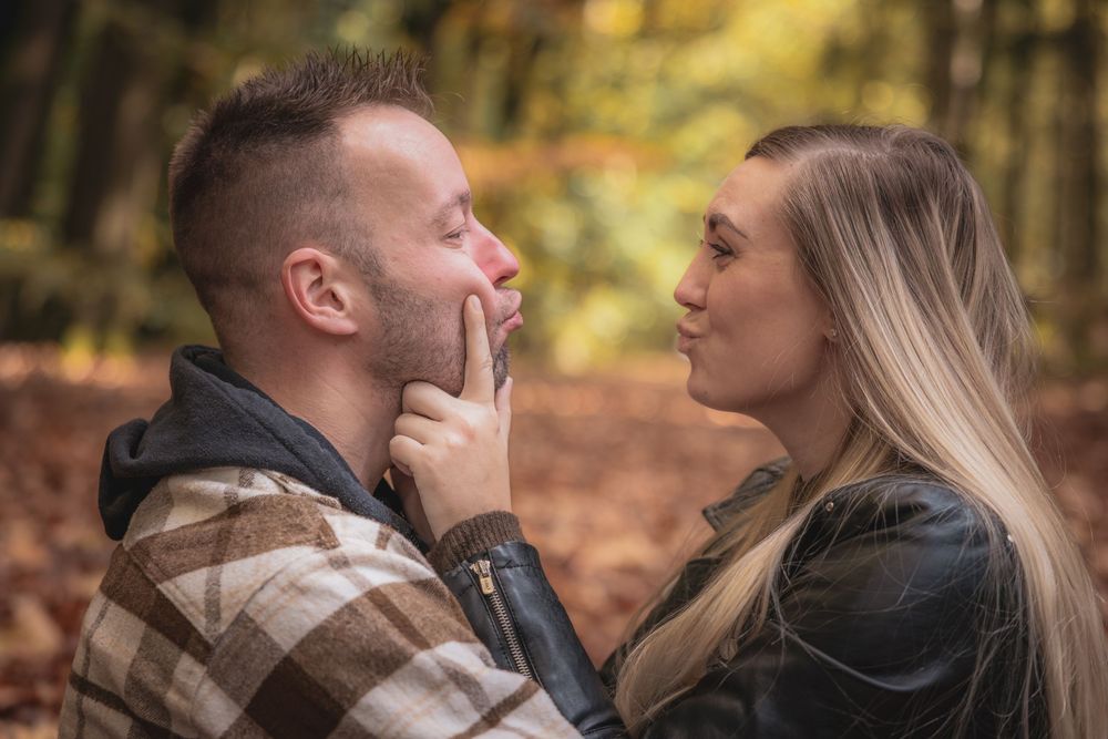 A couple shares romantic moments in an autumn forest setting during a photo session.