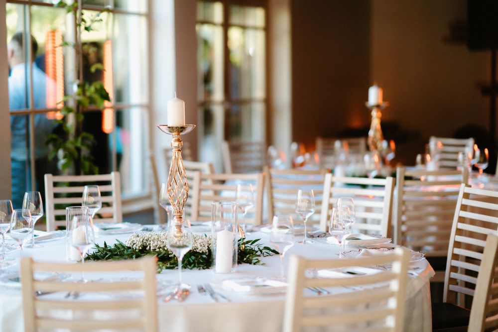 Elegant wedding reception table with white chairs and floral centerpieces in a bright venue.