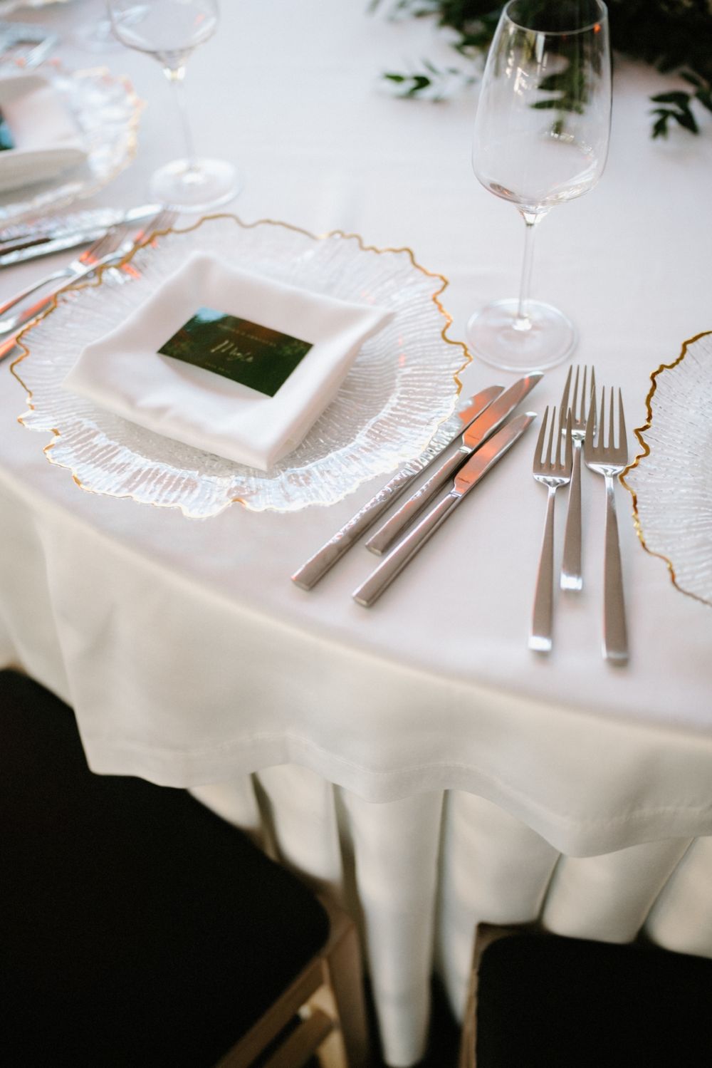 Elegant place setting with gold-rimmed plates, crystal stemware, and white tablecloth.