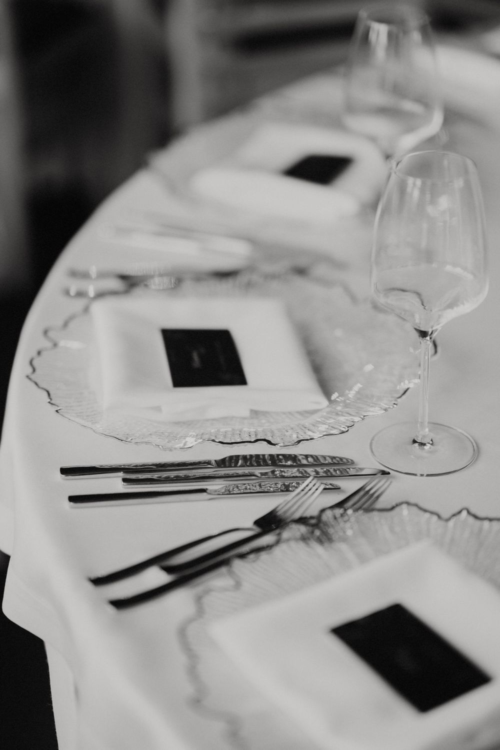 Elegant place setting with wine glass and silverware on white tablecloth in black and white.