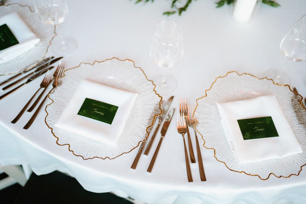 Wedding table settings with gold-rimmed plates and green name cards on white tablecloth.