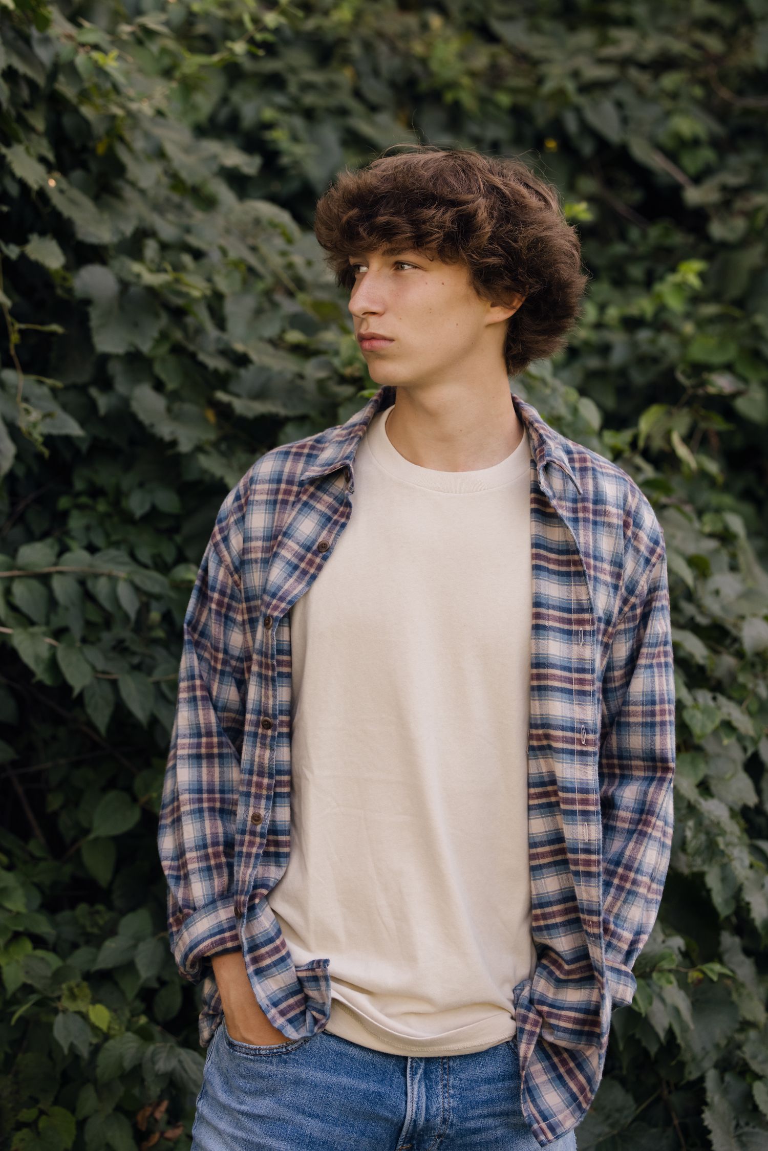 Relaxed outdoor portrait featuring plaid shirt and classic white tee against foliage.