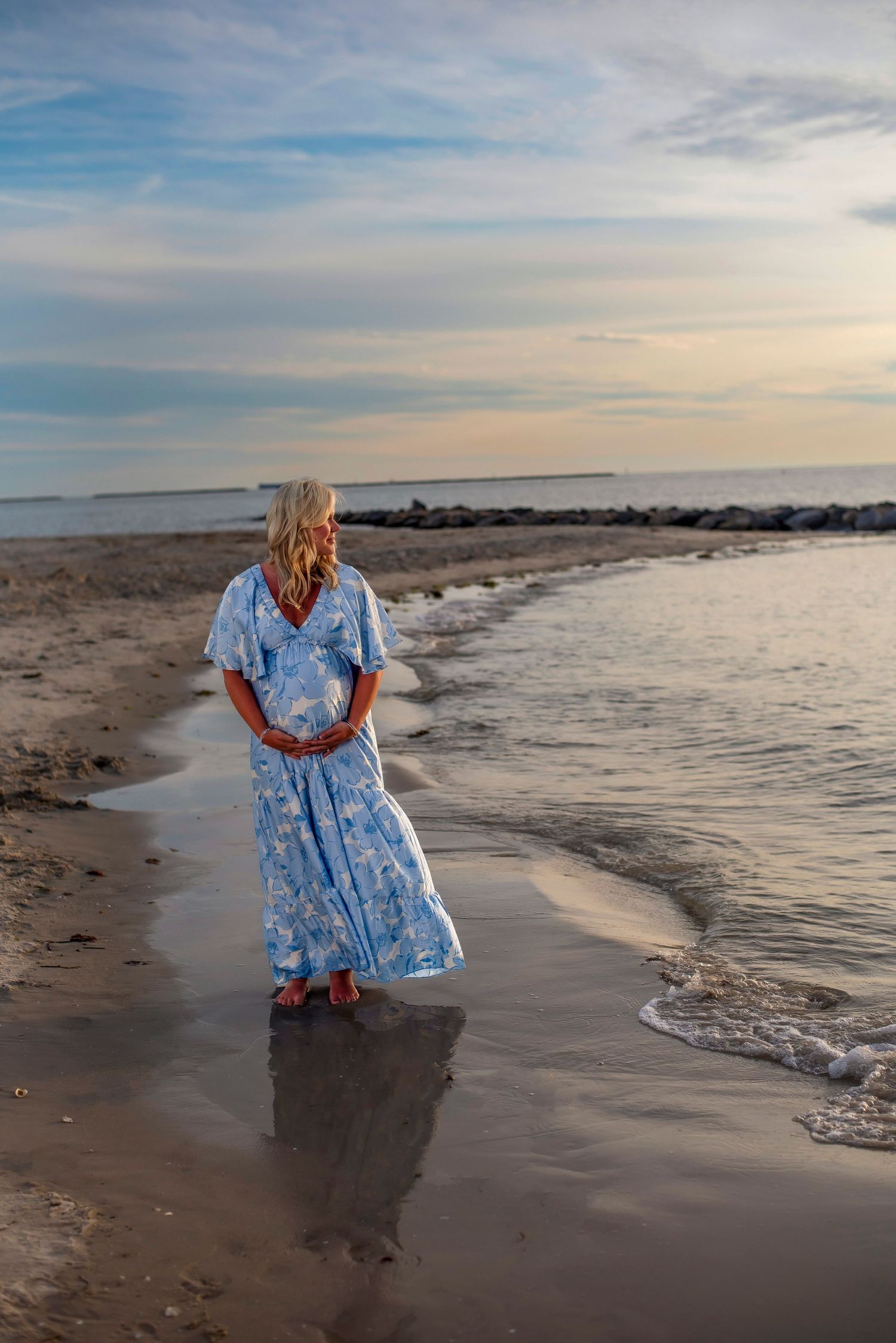 Maternity photo featuring woman in purple off-shoulder dress against white background.