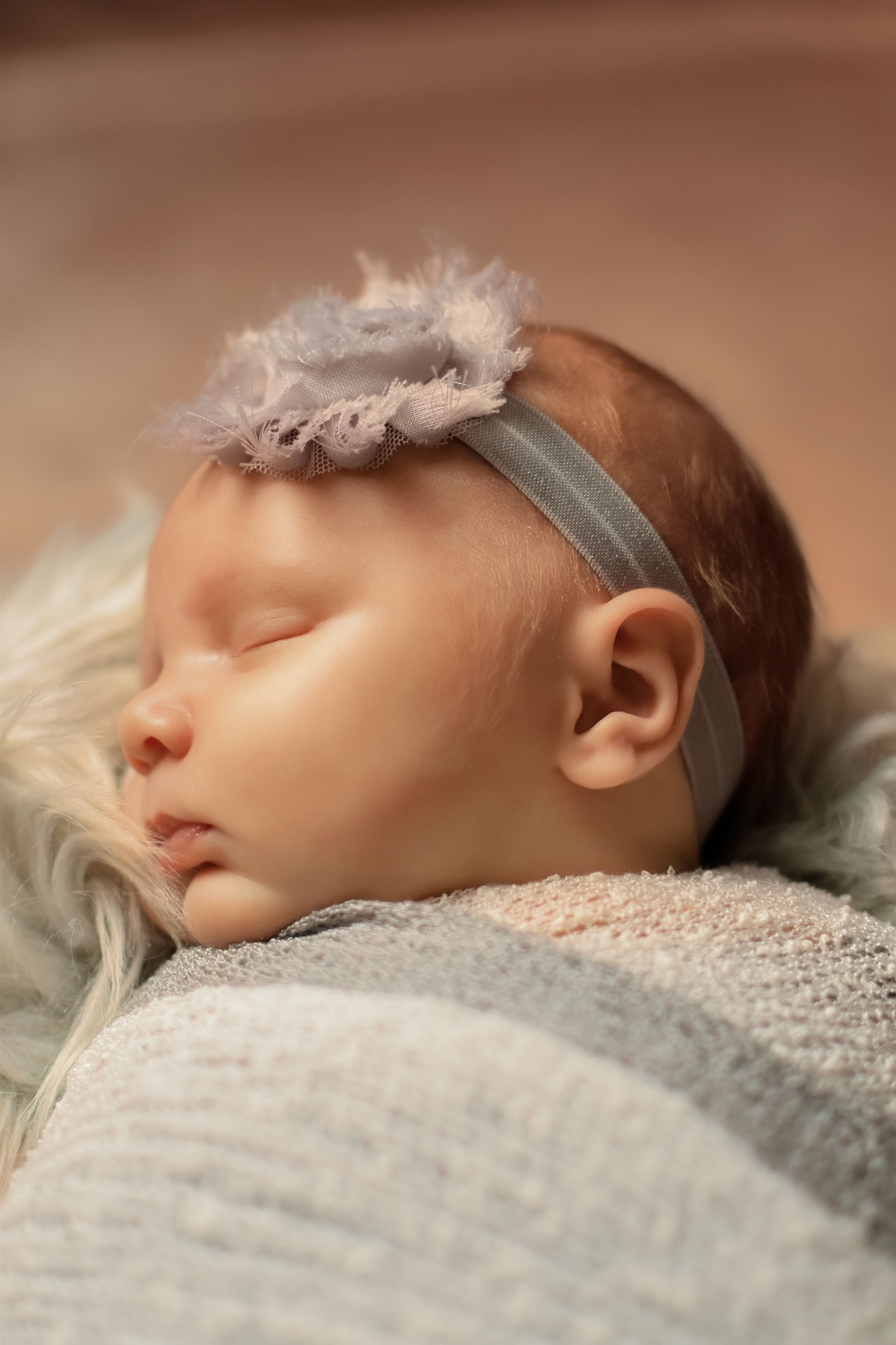 Peaceful sleeping newborn wearing gray headband on textured white blanket.