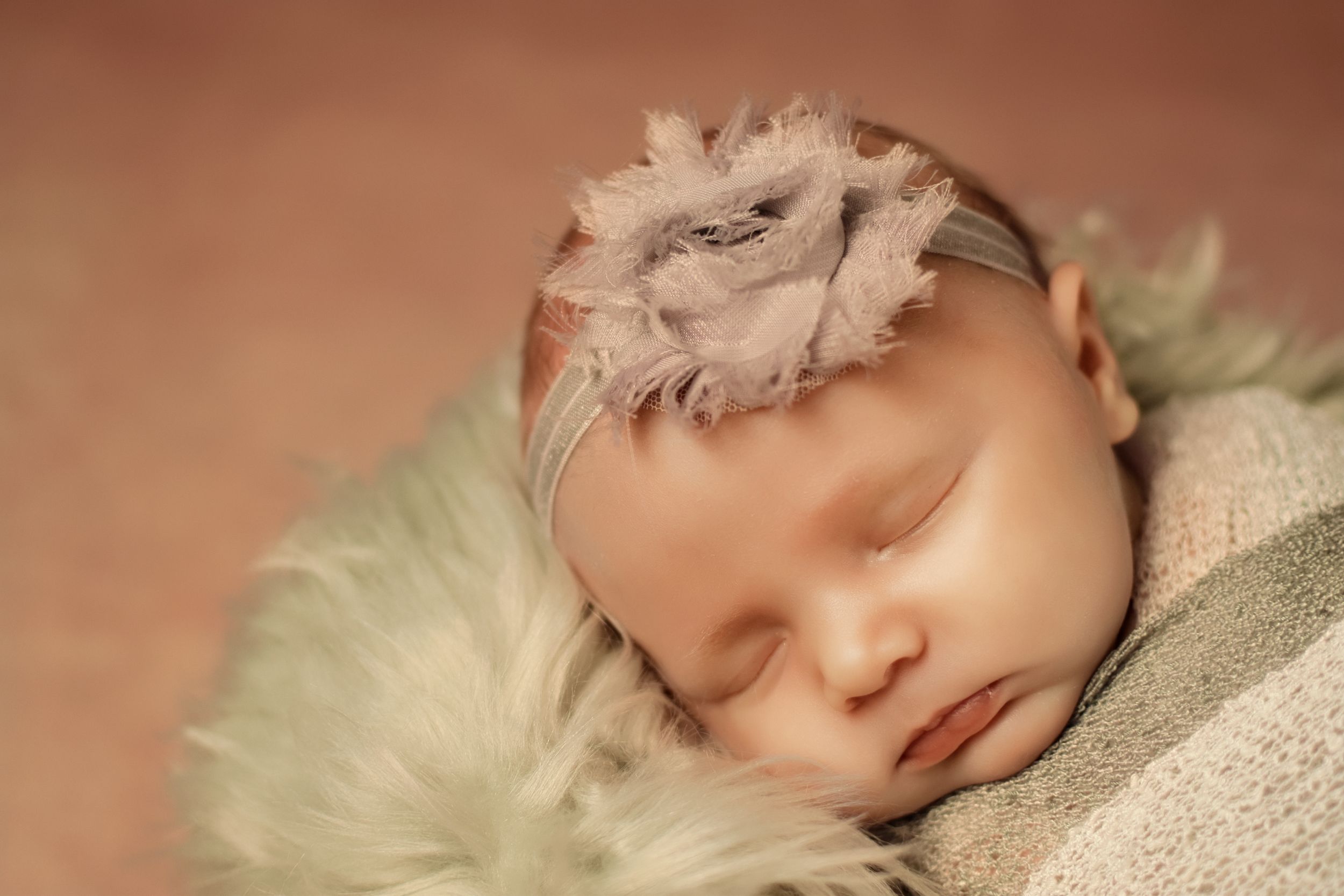 Newborn photography session featuring soft cream wraps and delicate floral accents on wooden backdrop.
