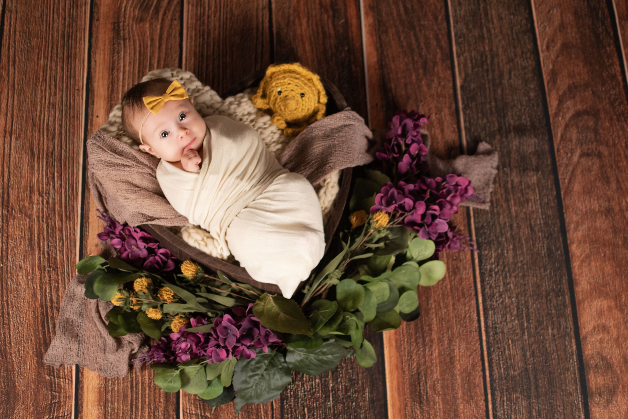 Artistic newborn photography with purple flowers and cream wraps on rustic wood background.