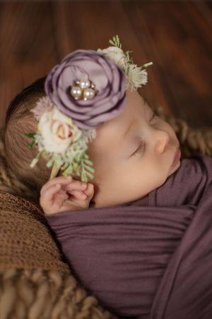 Artistic newborn portrait with purple floral headpiece and matching wrap.