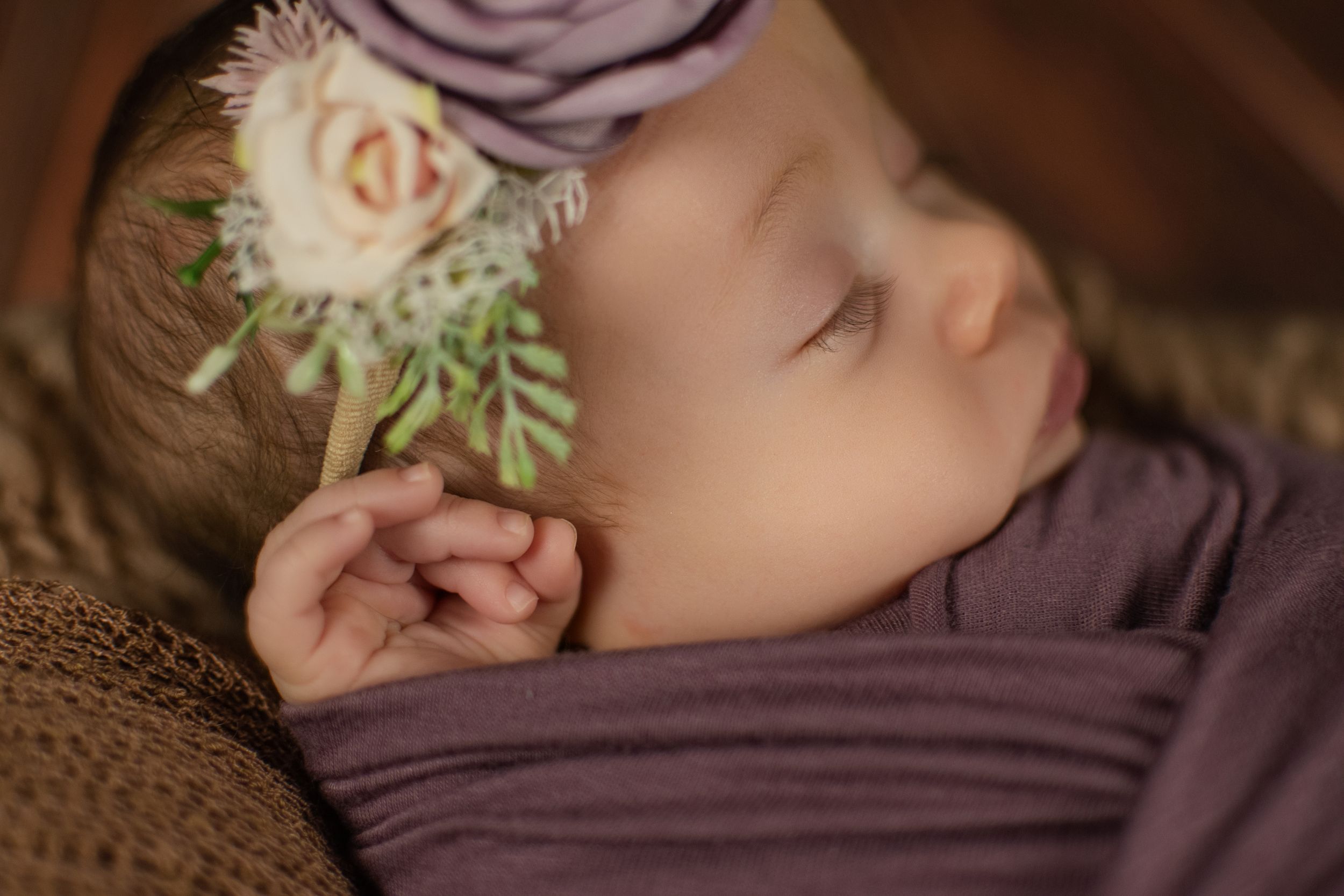 Peaceful sleeping newborn with delicate purple and white floral headpiece.