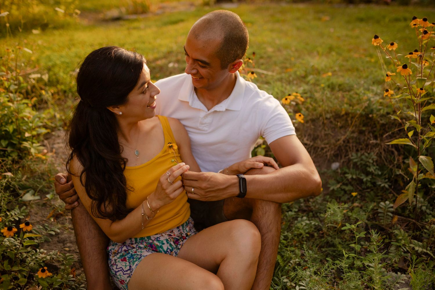 Couple sitting sweetly amongst black-eyed susans. He hands her a yellow flower at Lake Ontario Park, Kingston, Ontario, CA.