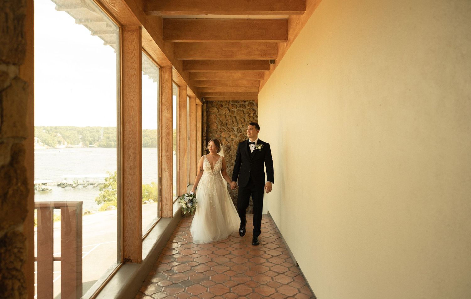 A couple walking down an open-air corridor with stone walls and wooden beams.
