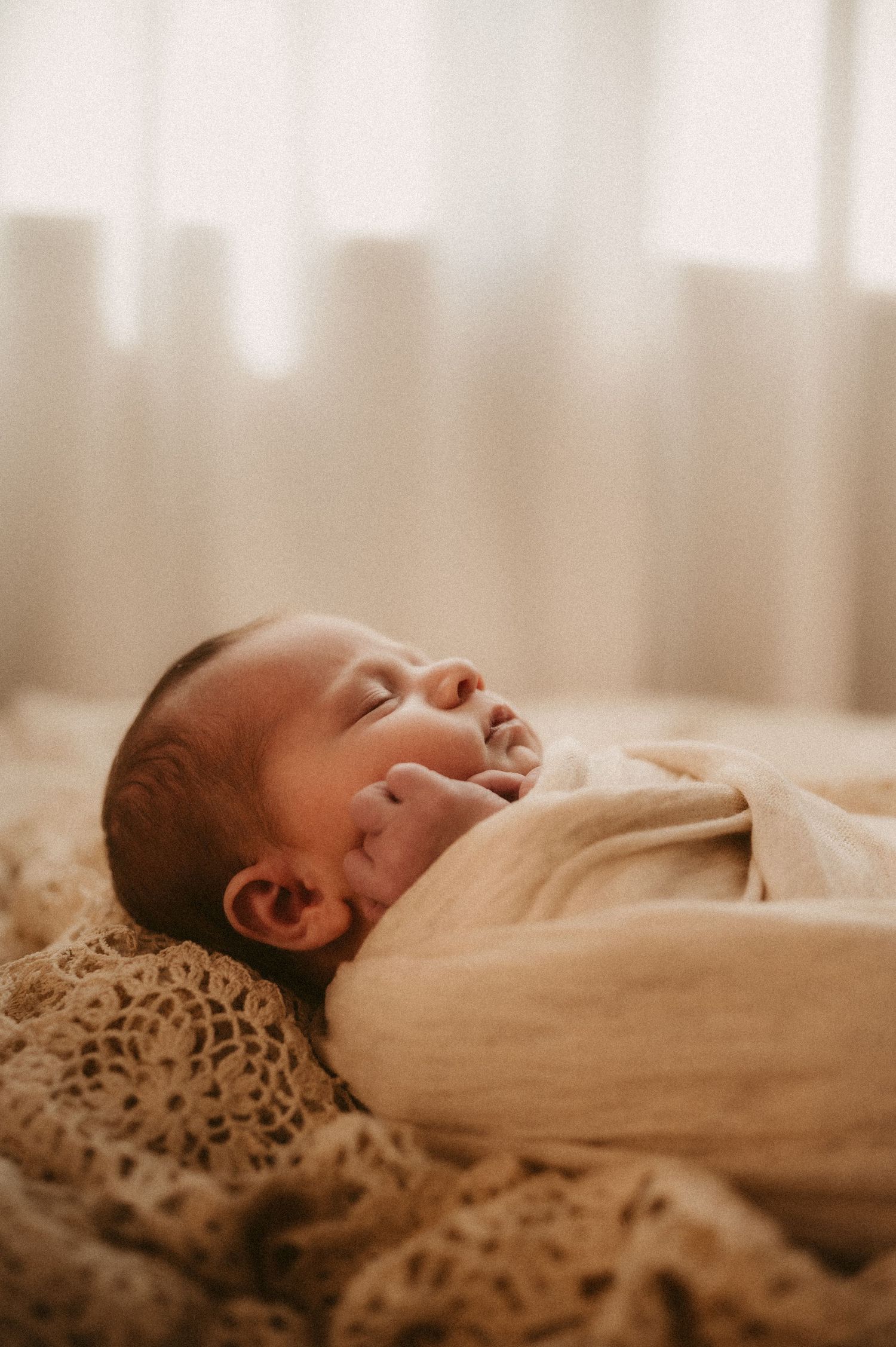 A sleeping newborn baby wrapped in soft cream fabric rests on a leopard print blanket in warm lighting.