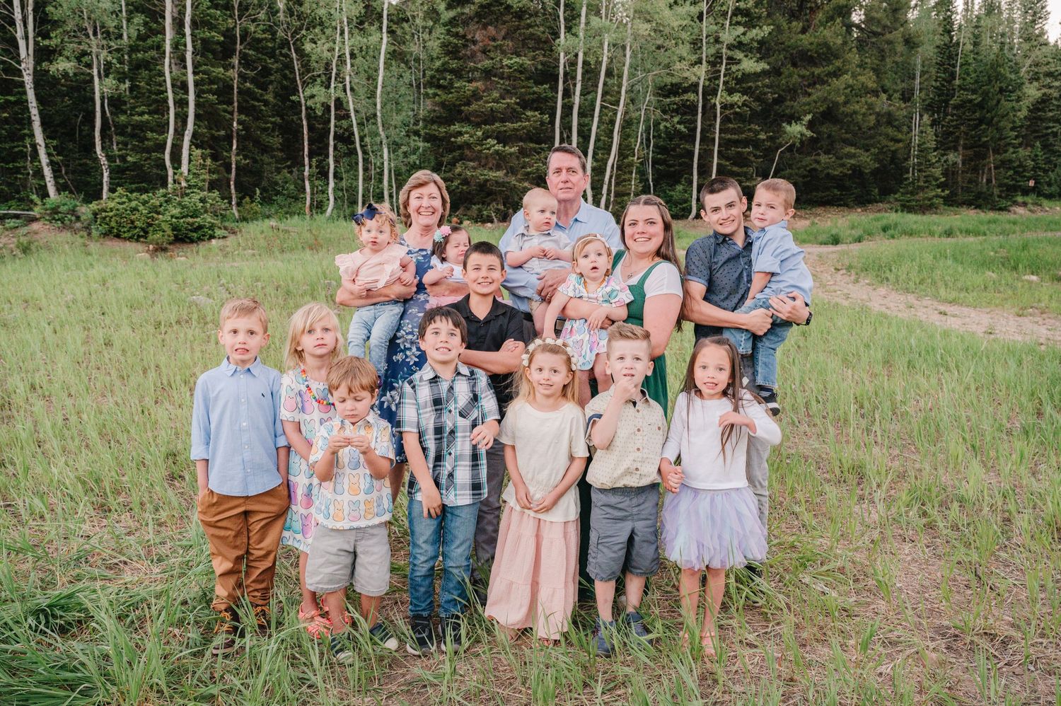 Group of children pose together in casual attire against backdrop of mountain forest.