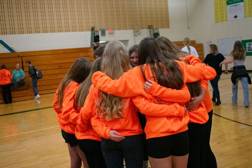 Prairie Farm Wisconsin Cross Country team 2024 huddled up in a circle with arms around each other.
