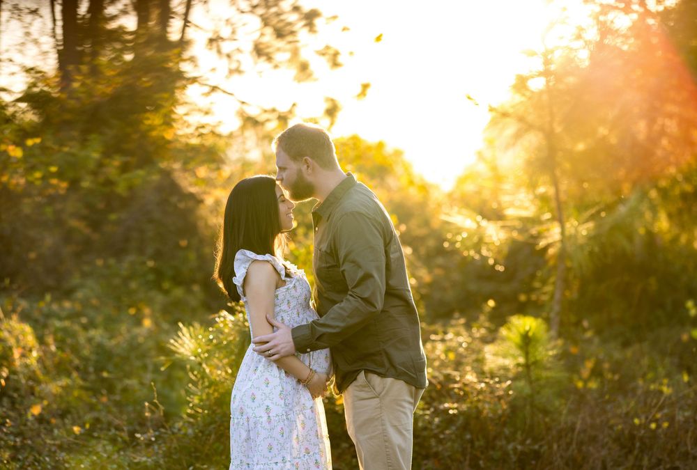 Couple sharing a romantic kiss at golden hour in a lush green outdoor setting with warm sunlight.