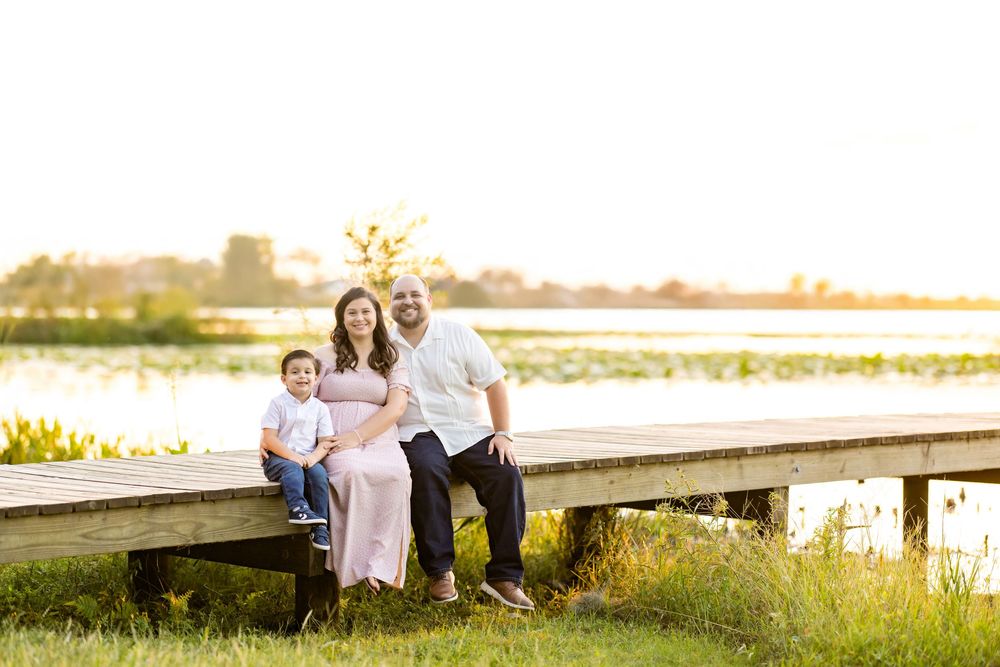 Family sits together on wooden dock during golden hour sunset at lakeside creating warm outdoor portrait moment.