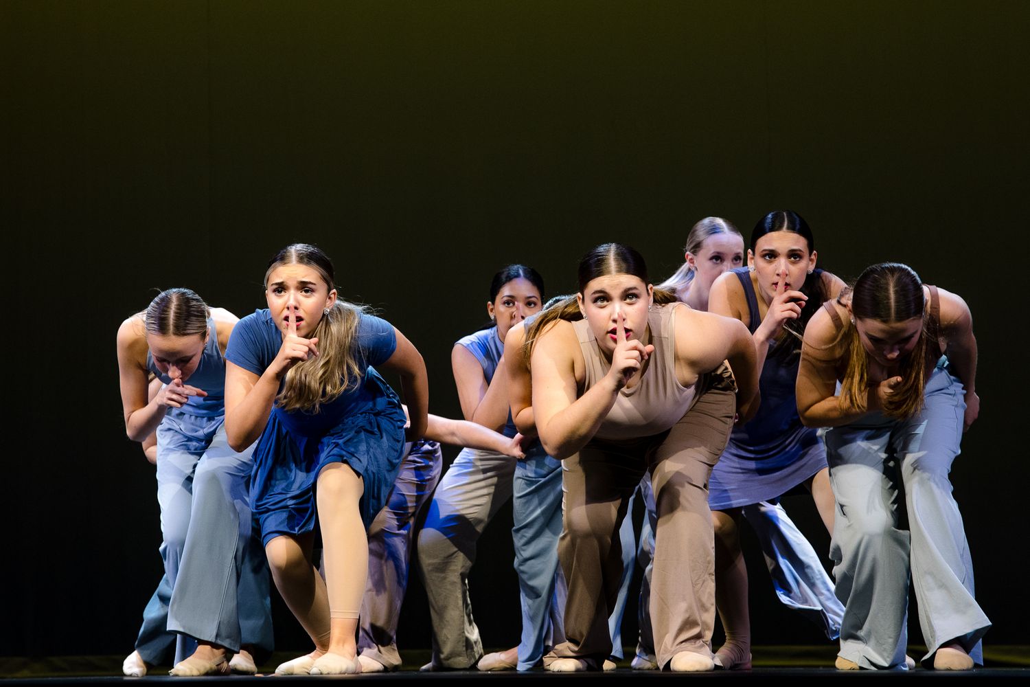 Modern dance group performs dramatic choreography in coordinated gray and blue costumes.