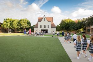 White church building with steeple on a green lawn with people walking along pathway.