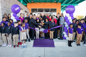 Ribbon cutting ceremony with purple balloons and students in uniforms at new facility entrance.