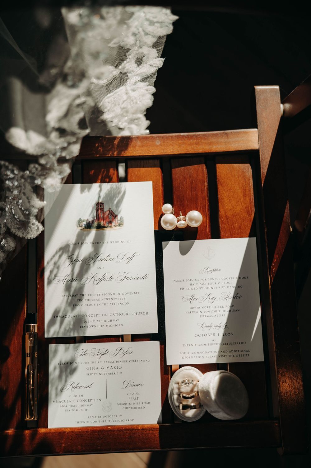 Elegant wedding invitation suite displayed on wooden chair with pearl earrings and ring box.