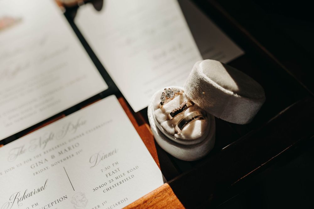 Wedding rings displayed in a velvet ring box alongside elegant calligraphy rehearsal dinner menus.