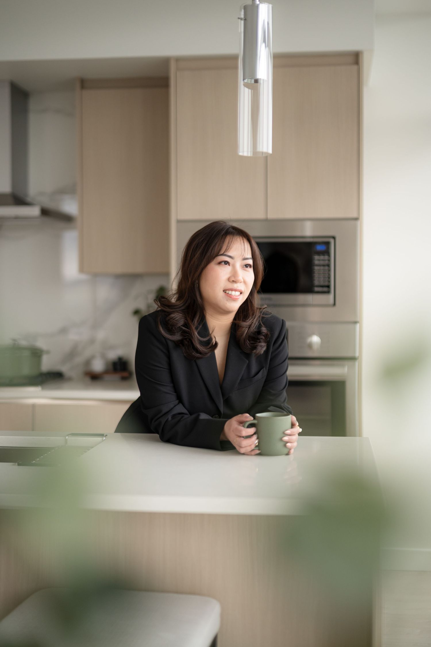 Professional wearing black blazer relaxes with coffee in modern kitchen with soft natural lighting and minimalist decor.