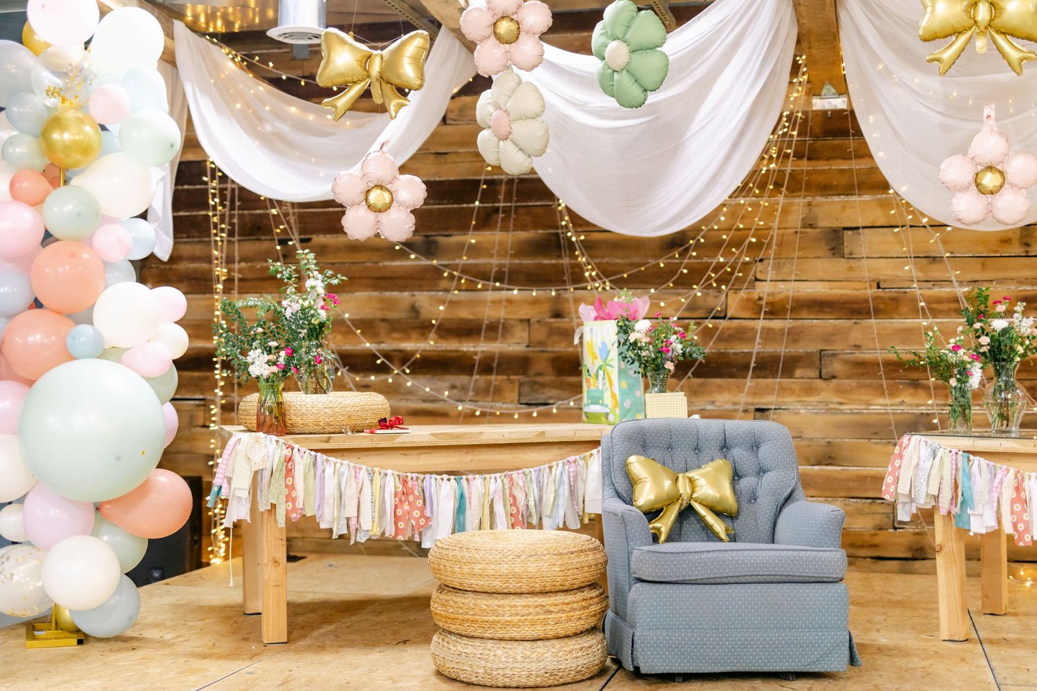 Rustic barn interior decorated with pastel balloons, floral accents, and white draping for party.