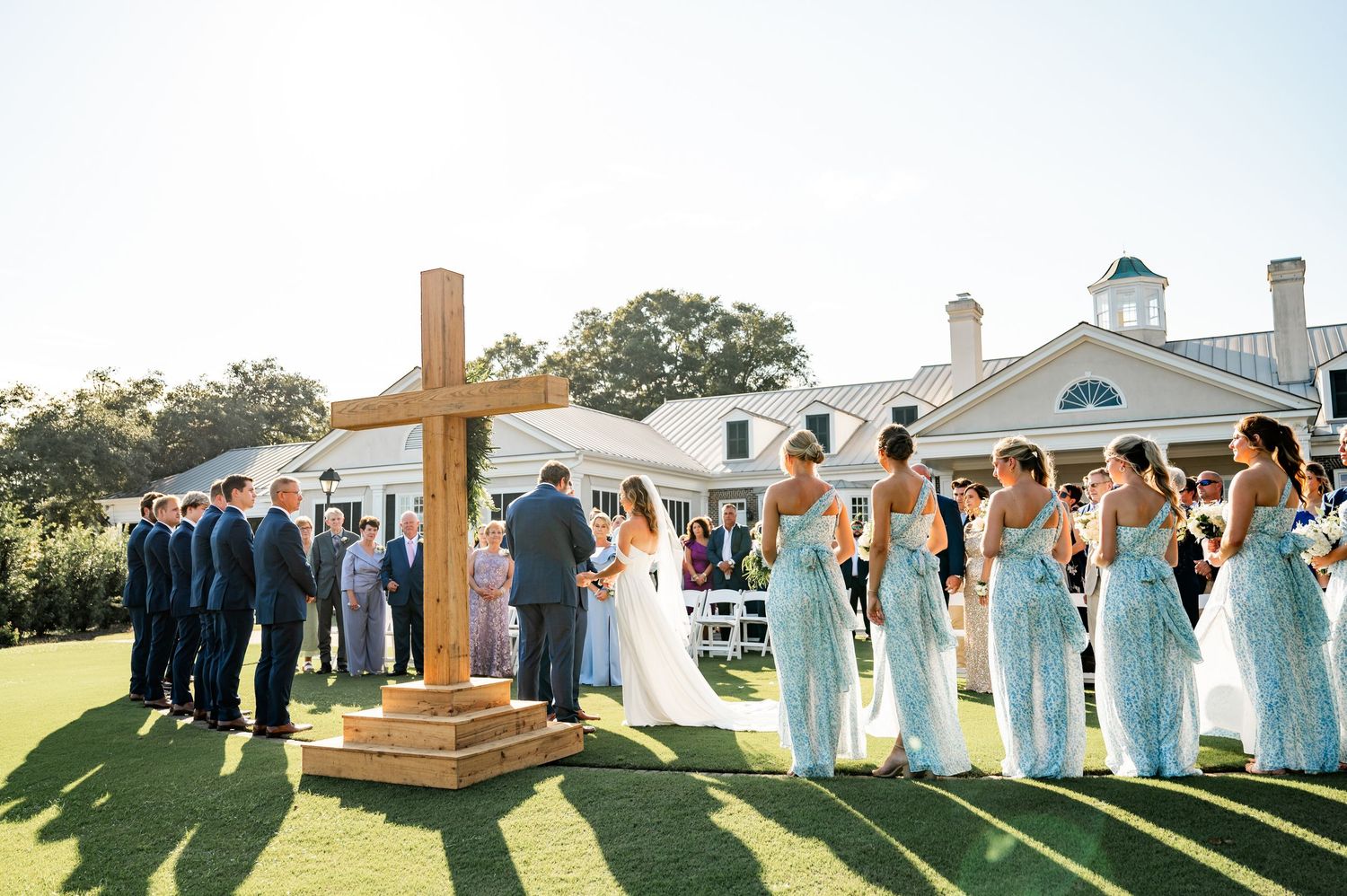 Wedding party members lined up outdoors with a white building in the background.
