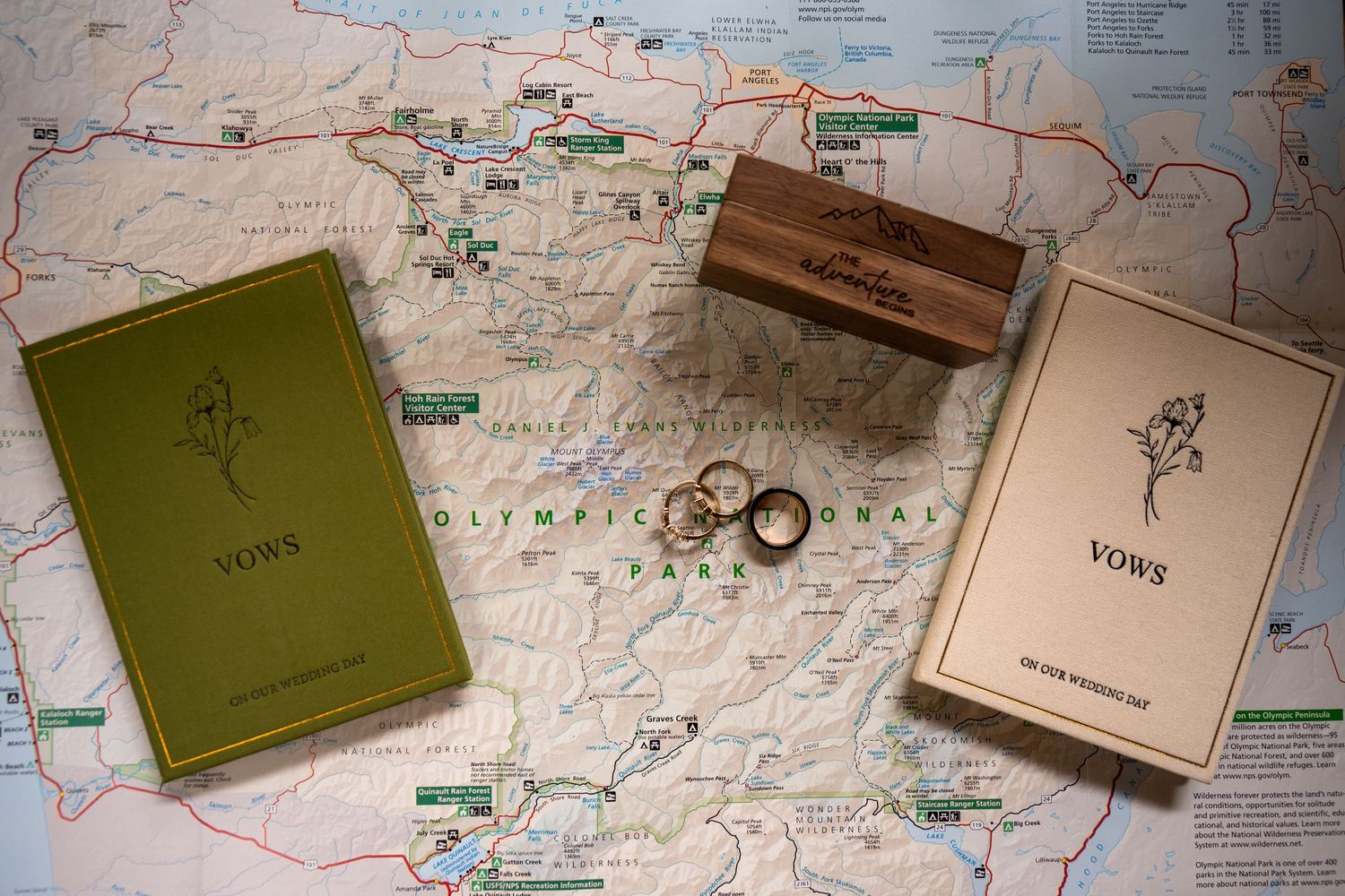 A map of Olympic National Park, overlayed with vow books and wedding rings from an adventure elopement set at Lake Crescent.