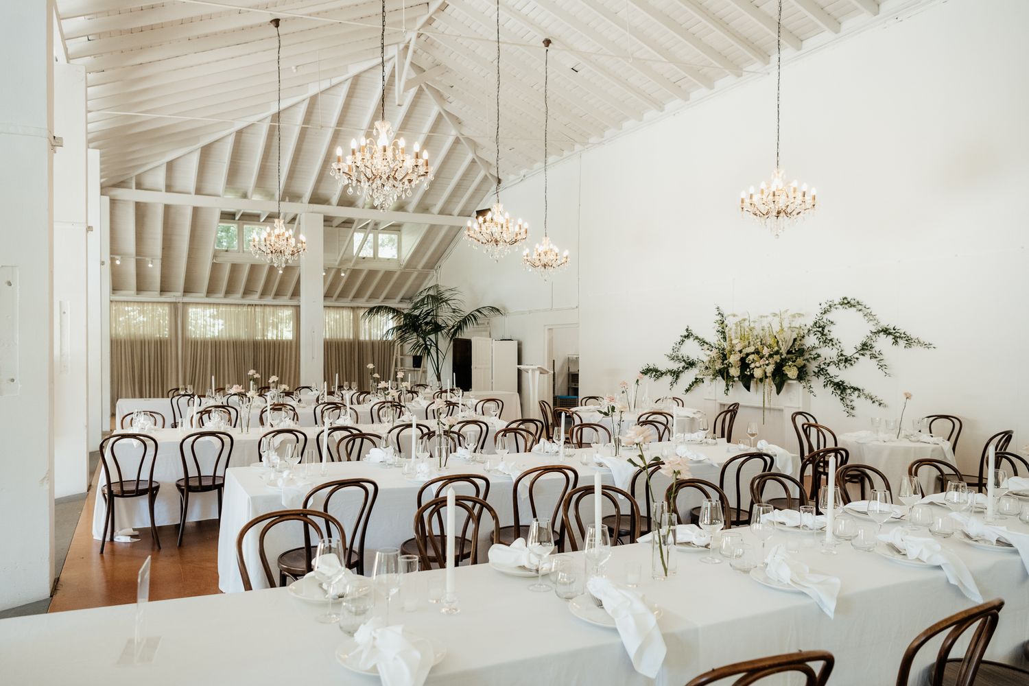 Elegant white wedding reception at Rose and Smith with wooden chairs, chandeliers, and vaulted ceilings captured by August and Vine