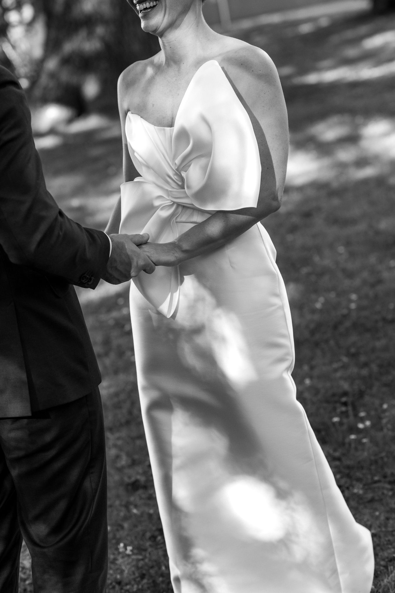 Black and white wedding photo showing details of a bride's white dress with large bow at the front  captured by August and Vine