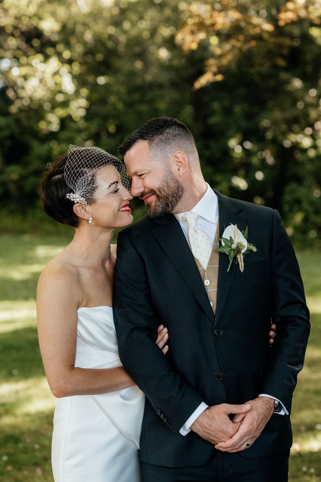 A joyful wedding couple share an intimate moment outdoors at Rose and Smith in a sunlit garden nook  captured by August and Vine