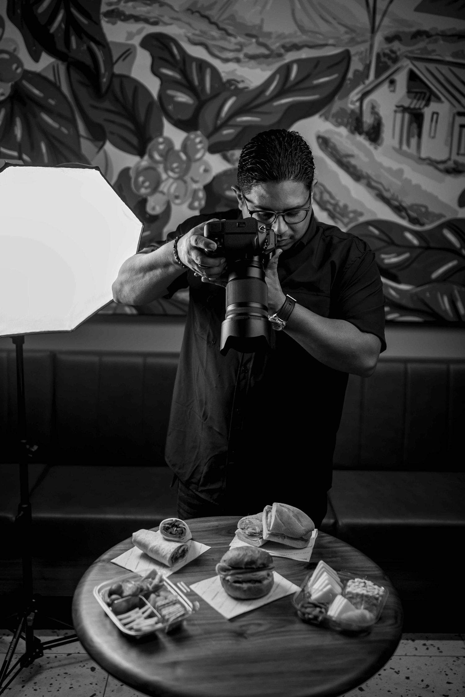 A black and white photo sequence showing someone taking photos of food and drinks on a round table at a restaurant.