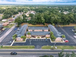Aerial view of commercial buildings and parking lots along a main road with surrounding trees.